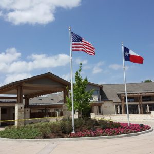 American and Texas flags flying outside a building under a blue sky.