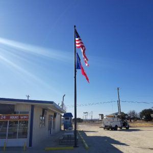American and Texas flags flying on a pole under a clear blue sky.