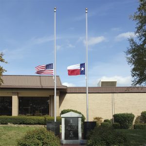 Flags of the USA and Texas at half-staff outside a building on a clear day.