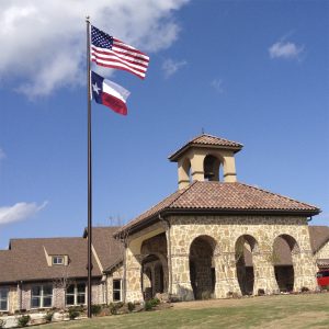 A building with a stone archway and two flags flying on a tall flagpole.