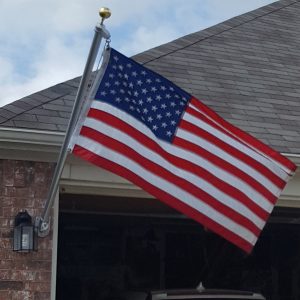 American flag waving outside a house against a cloudy sky.