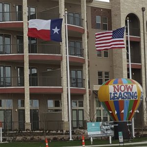 Texas and U.S. flags flying outside an apartment complex with a colorful hot air balloon decoration.