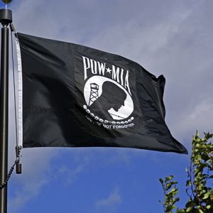 Black POW-MIA flag waving against a blue sky.