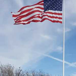 American flag waving against a blue sky with clouds.