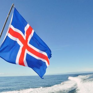 Icelandic flag waving against a clear blue sky by the sea.