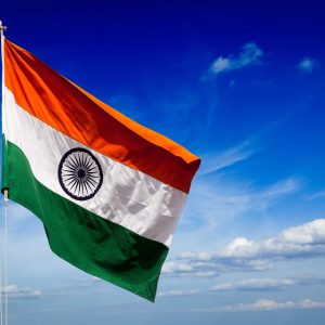The Indian national flag waving against a bright blue sky.