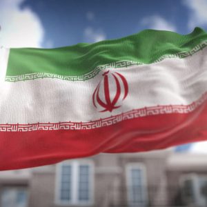 The Iranian flag waving against a blue sky with clouds.